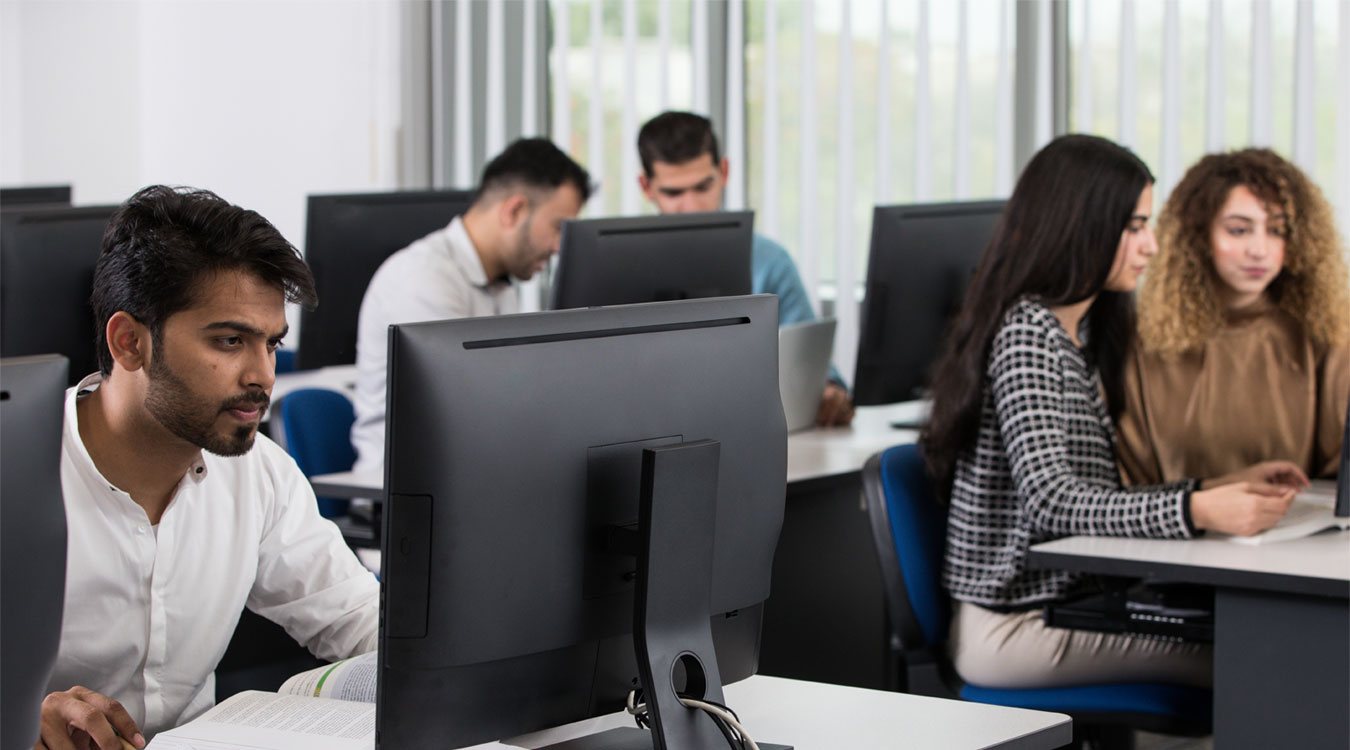 University students working on desktop computers in a modern computer lab setting.