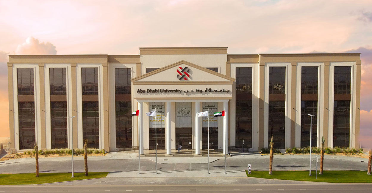 Front view of Abu Dhabi University campus building with UAE flags and clear sky