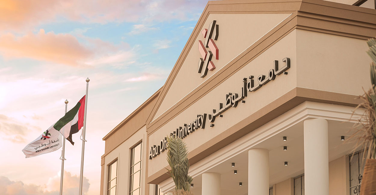 Abu Dhabi University main entrance with flags and soft evening sky in the background.