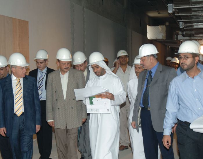 Delegation in hard hats reviewing construction plans during a site visit.