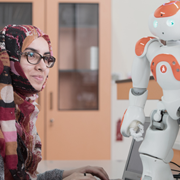 Female student interacting with humanoid robot during a robotics session in the lab setting.