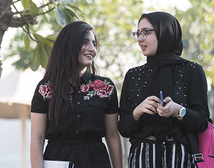 Two young women in conversation holding notebooks and smiling.