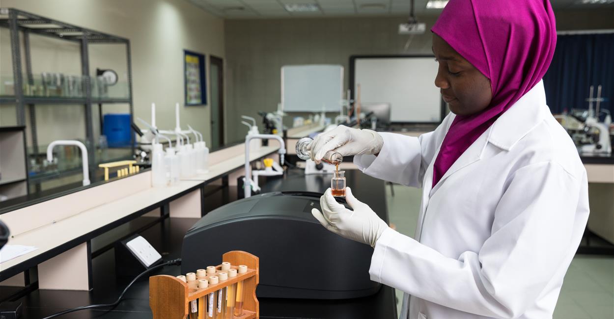 Female scientist in lab coat pouring liquid into vial during chemistry experiment in lab