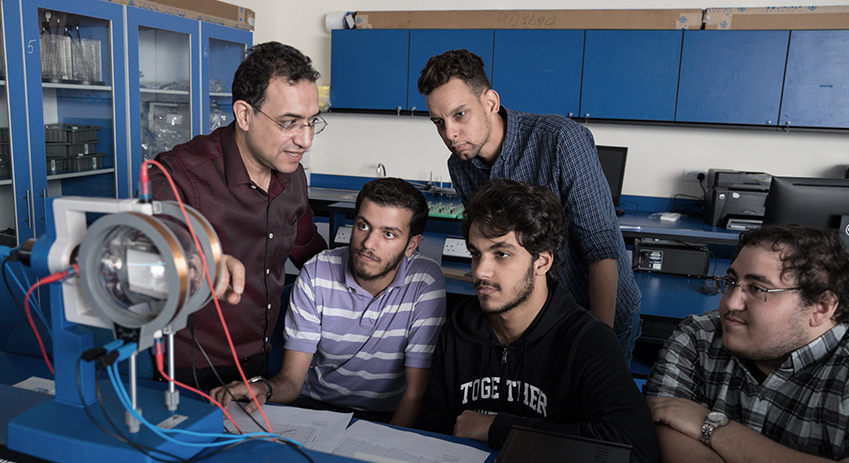 Four Bachelor of Science in Electrical Engineering students at Abu Dhabi University and their professor discussing a project