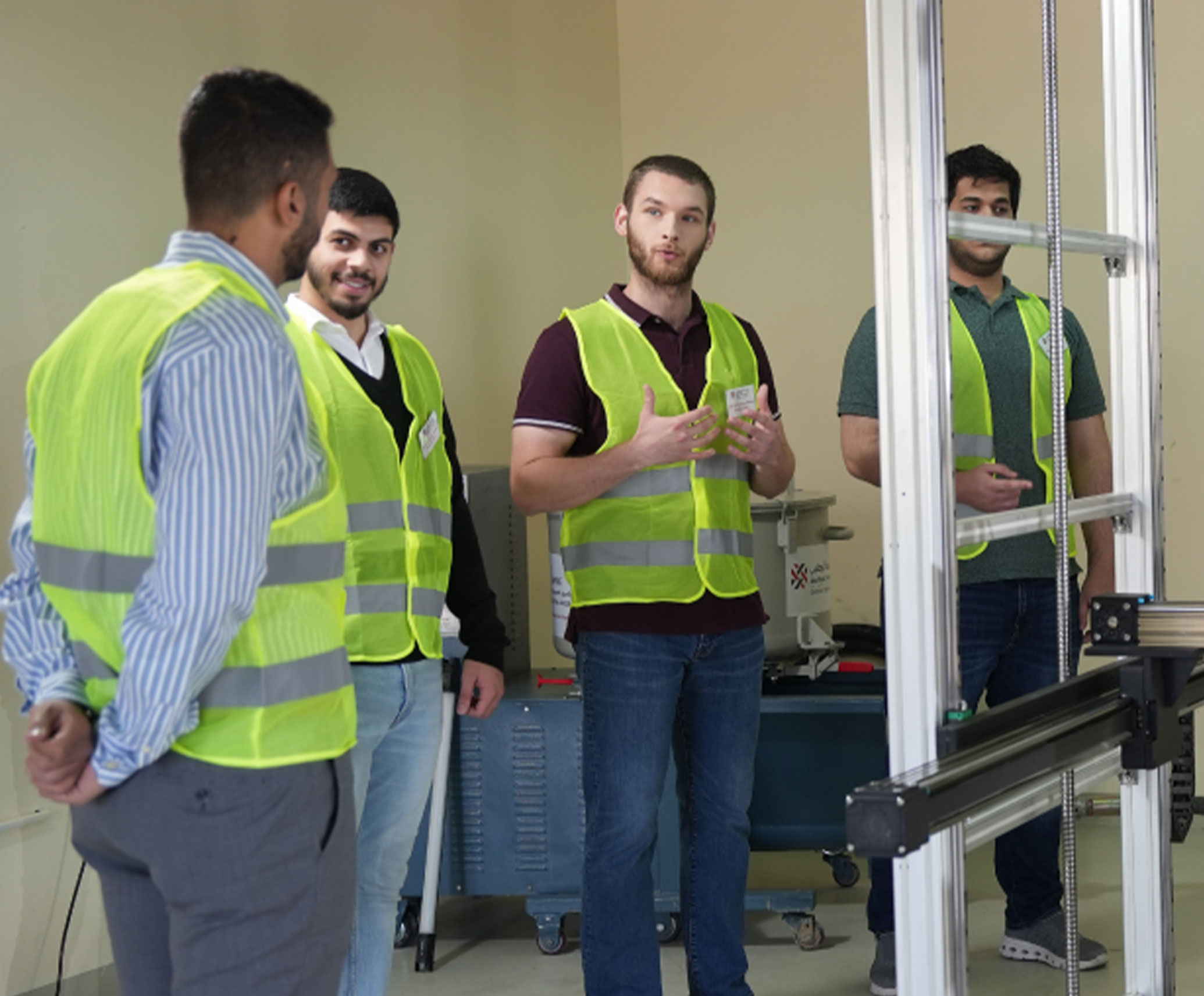 Engineering students in safety vests engaged in a hands-on classroom discussion on machinery and innovation.