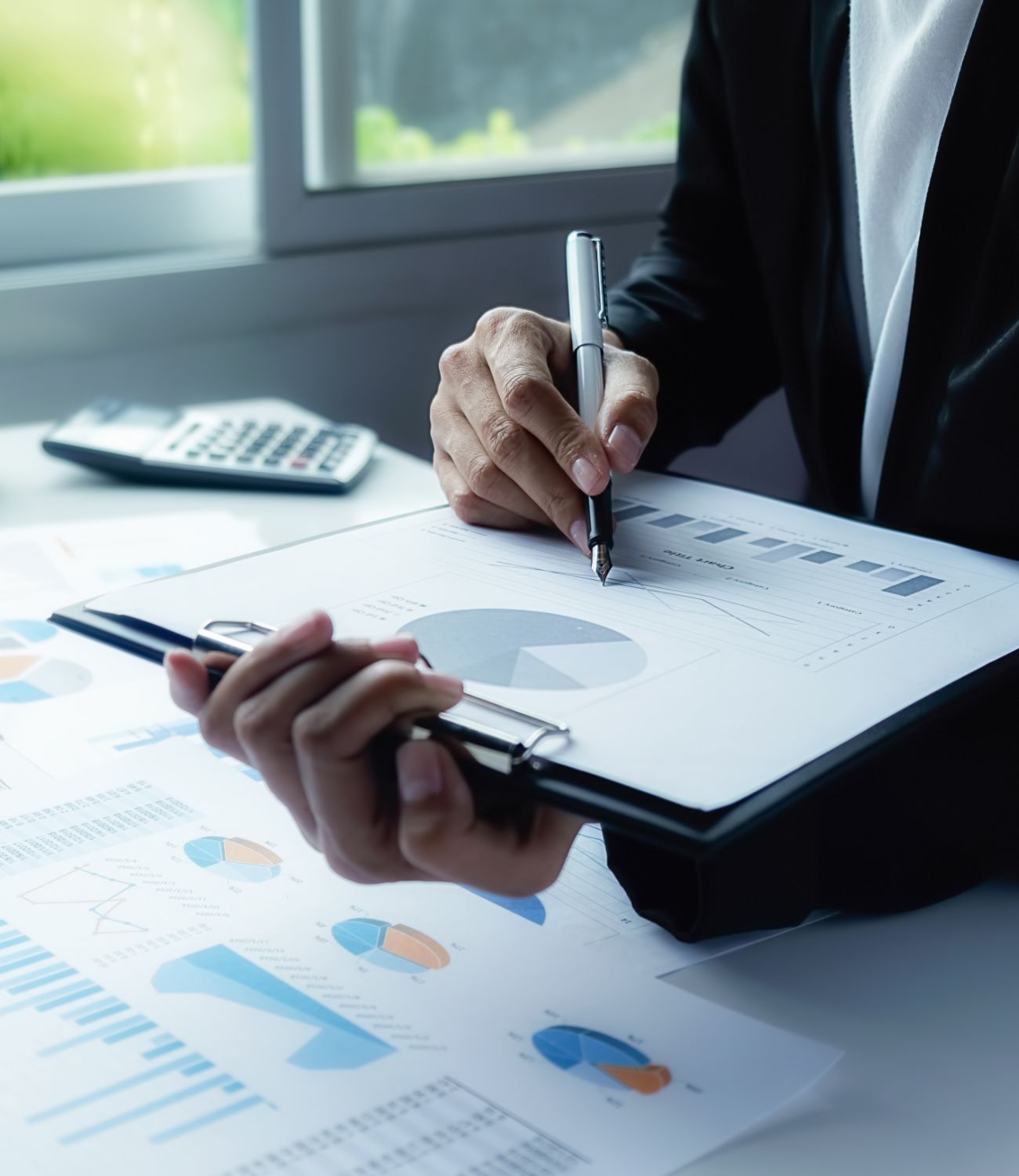 Group of professionals in formal attire collaborating around a laptop in a bright modern office.