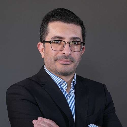 Academic portrait of professor in a dark suit and glasses against a gray background